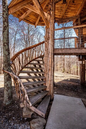 A wooden spiral staircase leading to a covered area with a view of trees and sky.