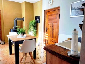 A dining area with a table, chairs, a potted plant, a wooden door, and a wall clock.