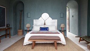 A bedroom with a large bed, wooden bench, and a view of the outdoors.