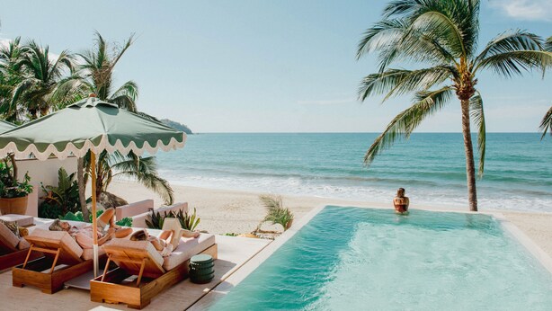A beachside pool area with lounge chairs and a palm tree.