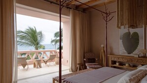 A bedroom with a large bed, a view of the ocean, and a balcony with chairs.