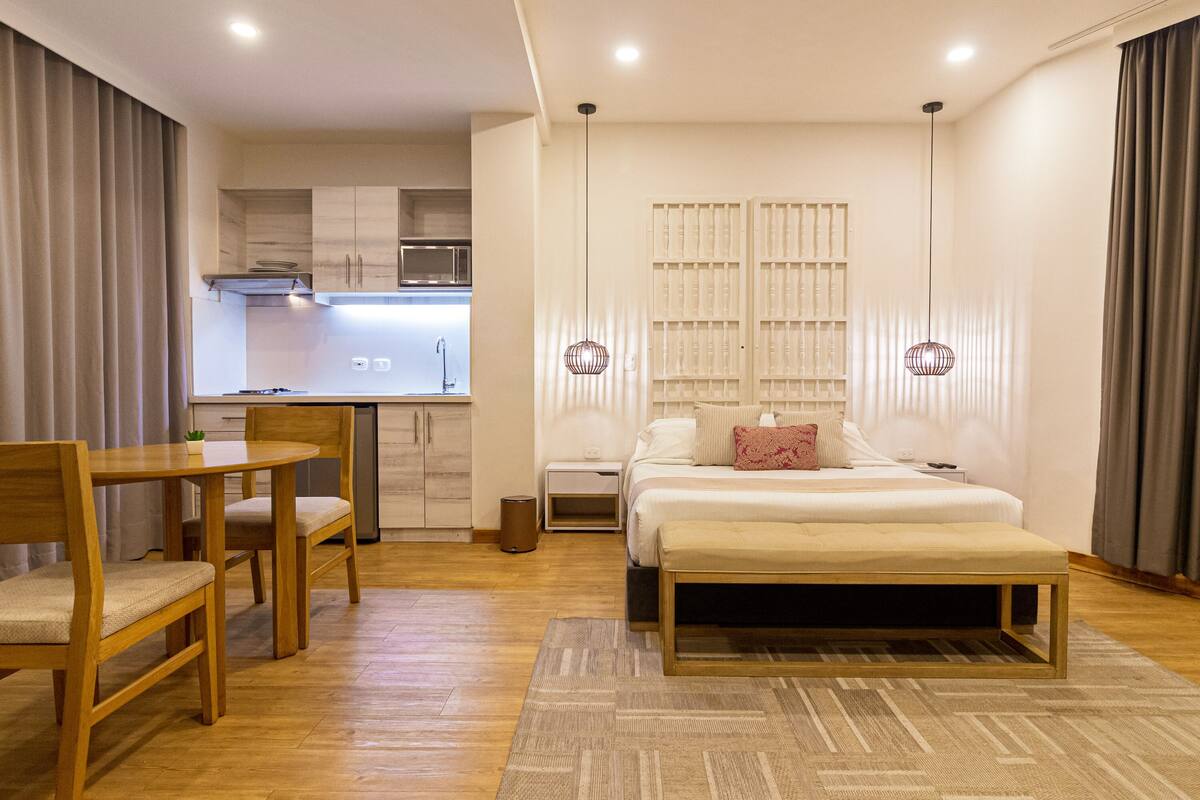 Un dormitorio moderno con cama, mesitas de noche, escritorio y kitchenette.