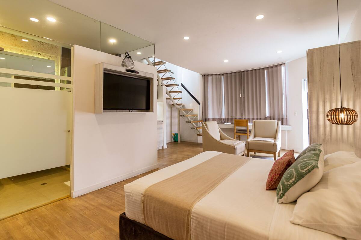 Una habitación de hotel moderna con cama, televisor, una escalera y una zona de estar.