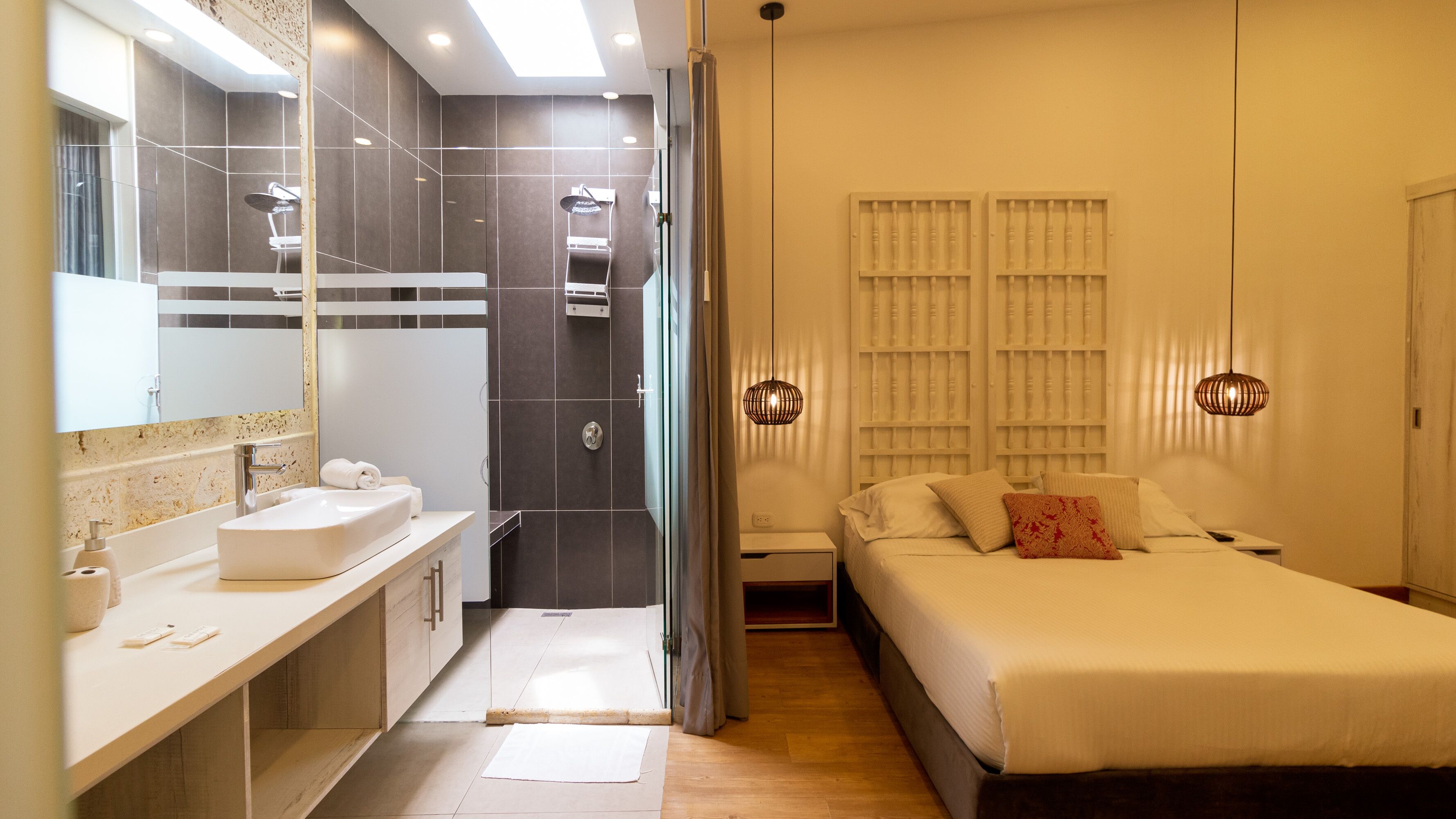 A modern hotel room with a bathroom, a shower, a bed with pillows, and a bedside table.