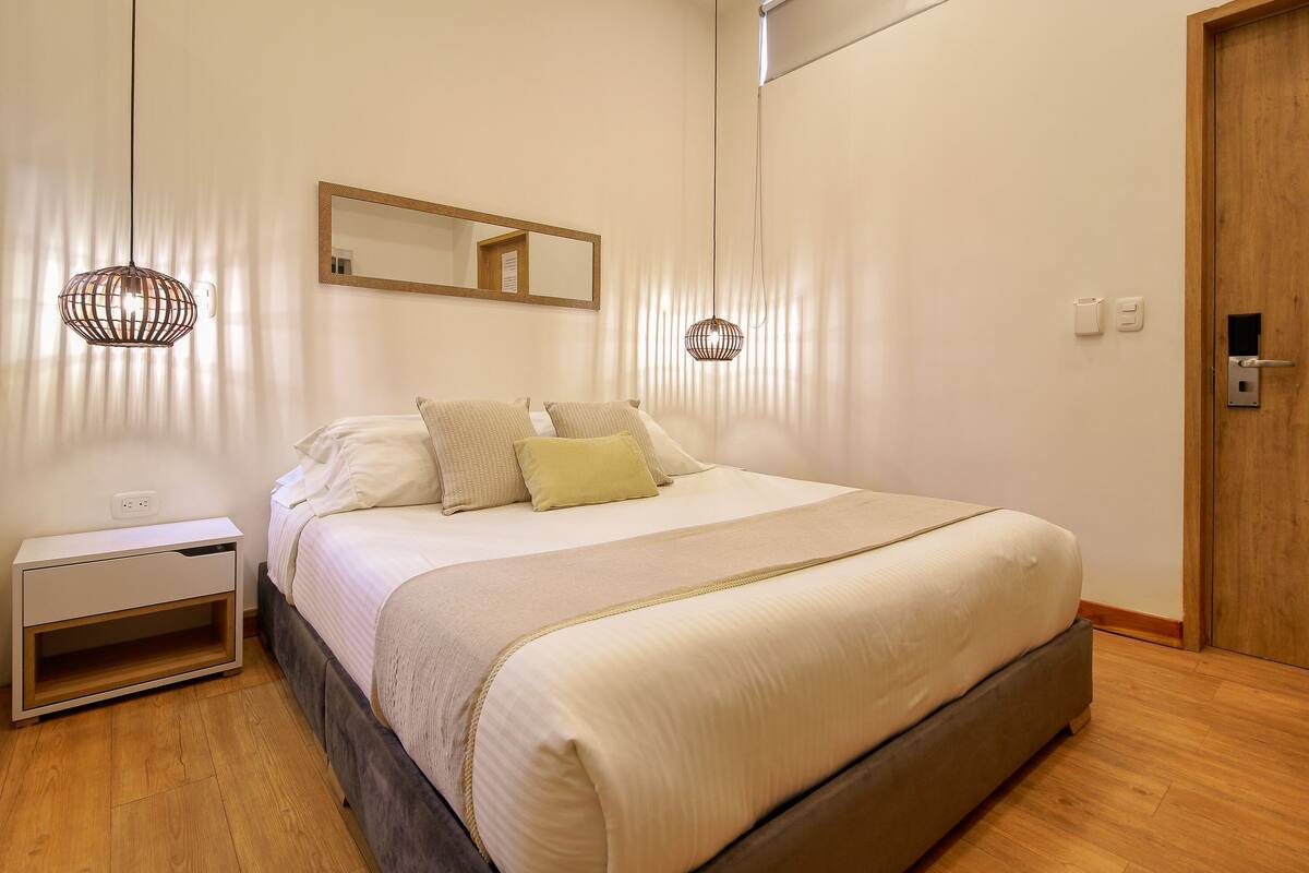 Un dormitorio con cama, mesitas de noche, un espejo y una puerta.