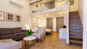 A modern hotel room with a sofa, armchairs, a small table, a staircase, and a balcony.