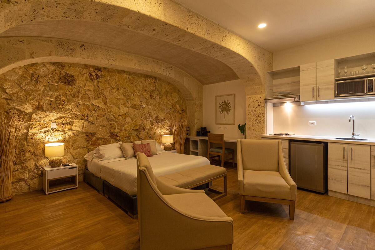 Un dormitorio acogedor con pared de piedra, una cama, mesitas de noche y una silla.