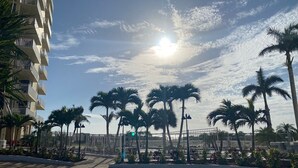 A paved walkway lined with palm trees and a white fence, leading to a building with balconies. - Fantastic Ft Myers Beachfront Condo! Flexible Check-in Dates and many amenities! (Fort Myers Beach)