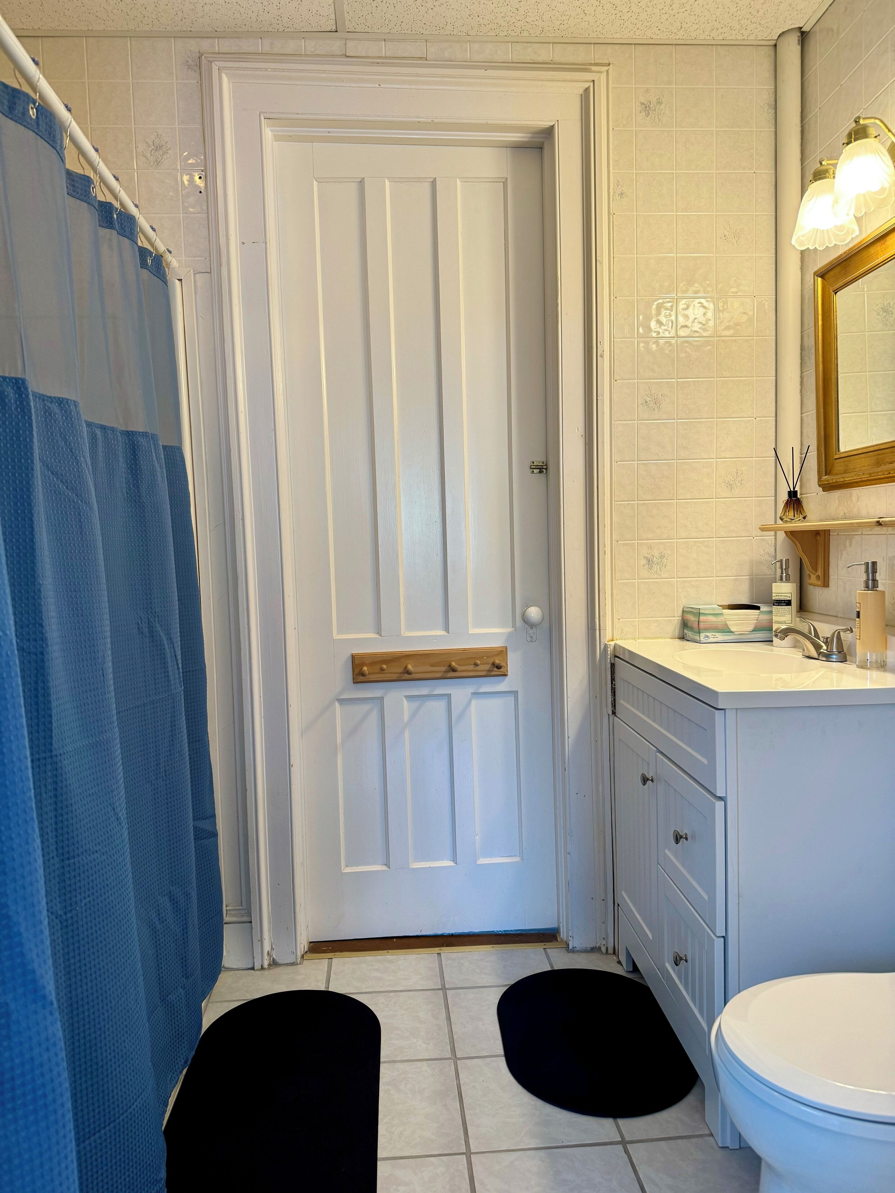 A bathroom with a white door, a blue shower curtain, a sink with a mirror, and a toilet.