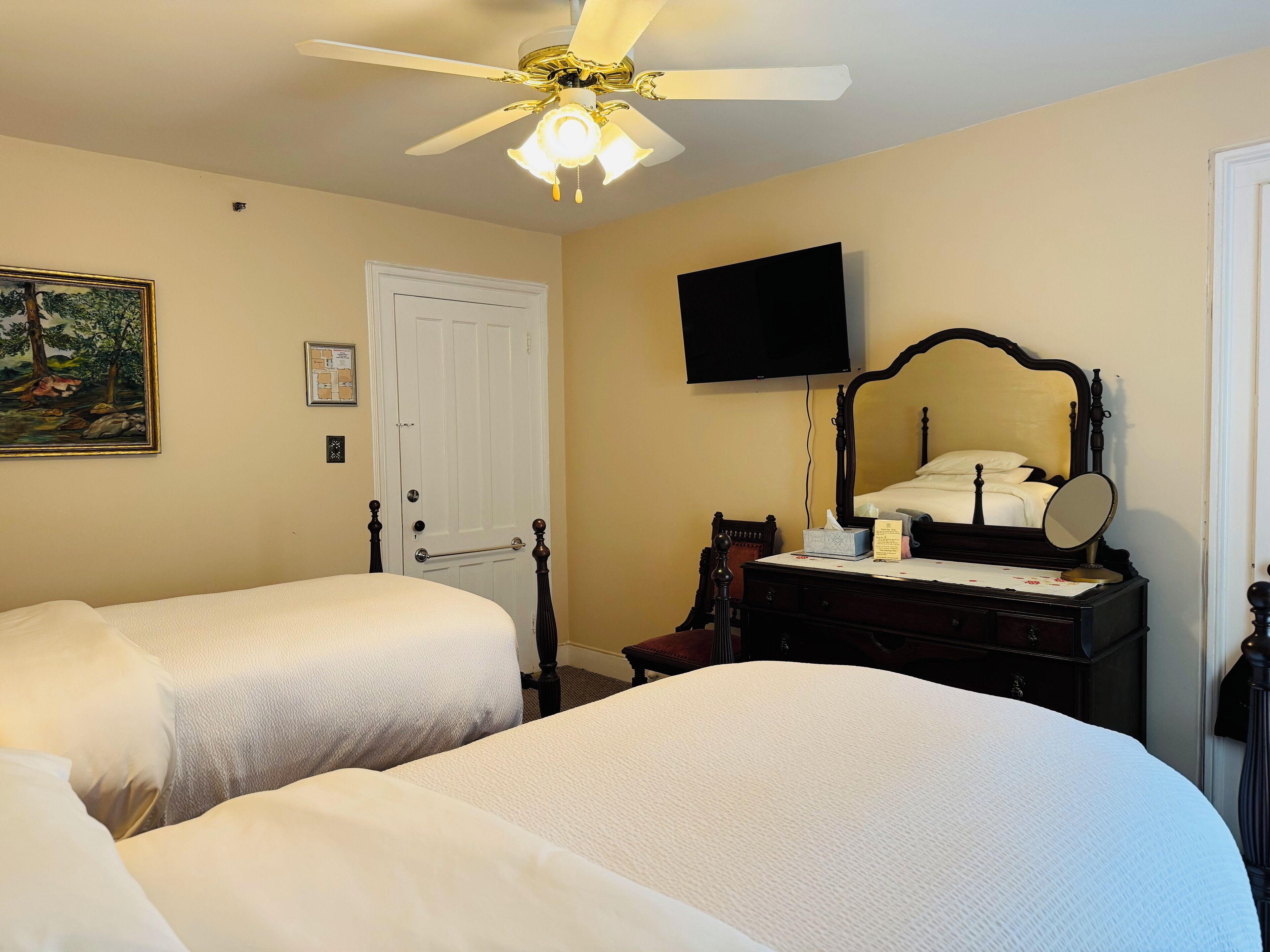 A hotel room with two beds, a ceiling fan, a mounted TV, a dresser with a mirror, and a door.