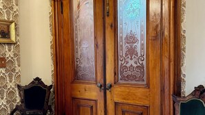 Ein Zimmer mit einer großen Holztür mit aufwendigen Verzierungen, zwei stilsicheren Sesseln mit grüner Polsterung und Wandpapier mit Muster.