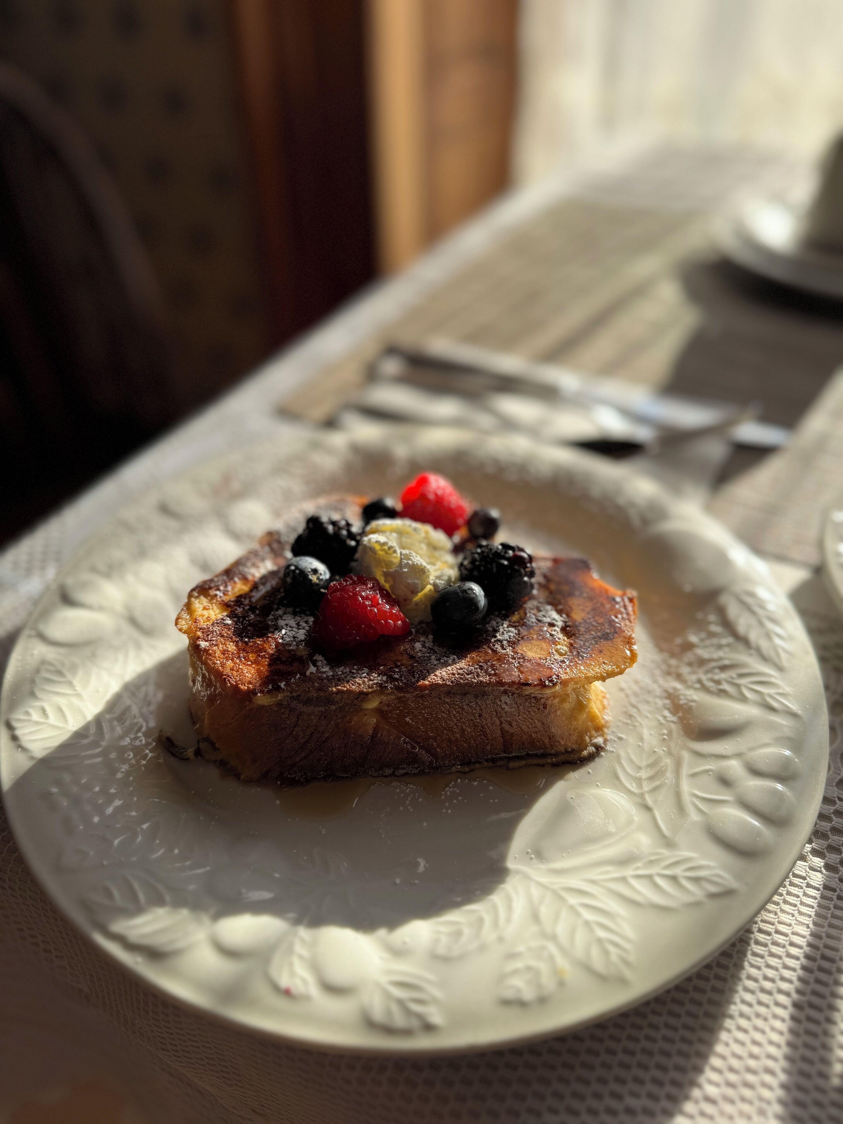 A dessert on a white plate with a floral pattern, featuring a piece of toast topped with berries and powdered sugar.