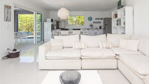 A modern living room with a white sectional sofa, a dining area with a glass table, and a kitchen in the background.