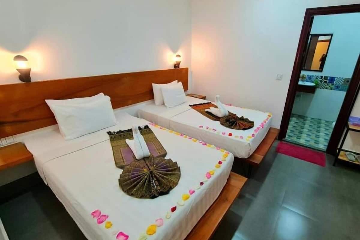 A hotel room with two beds, each with a decorative swan centerpiece, white bedding, and wall-mounted lights.