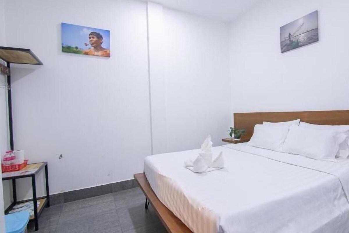 Een hotelkamer met een bed, een nachtkastje met een plant en twee aan de muur hangende foto's.
