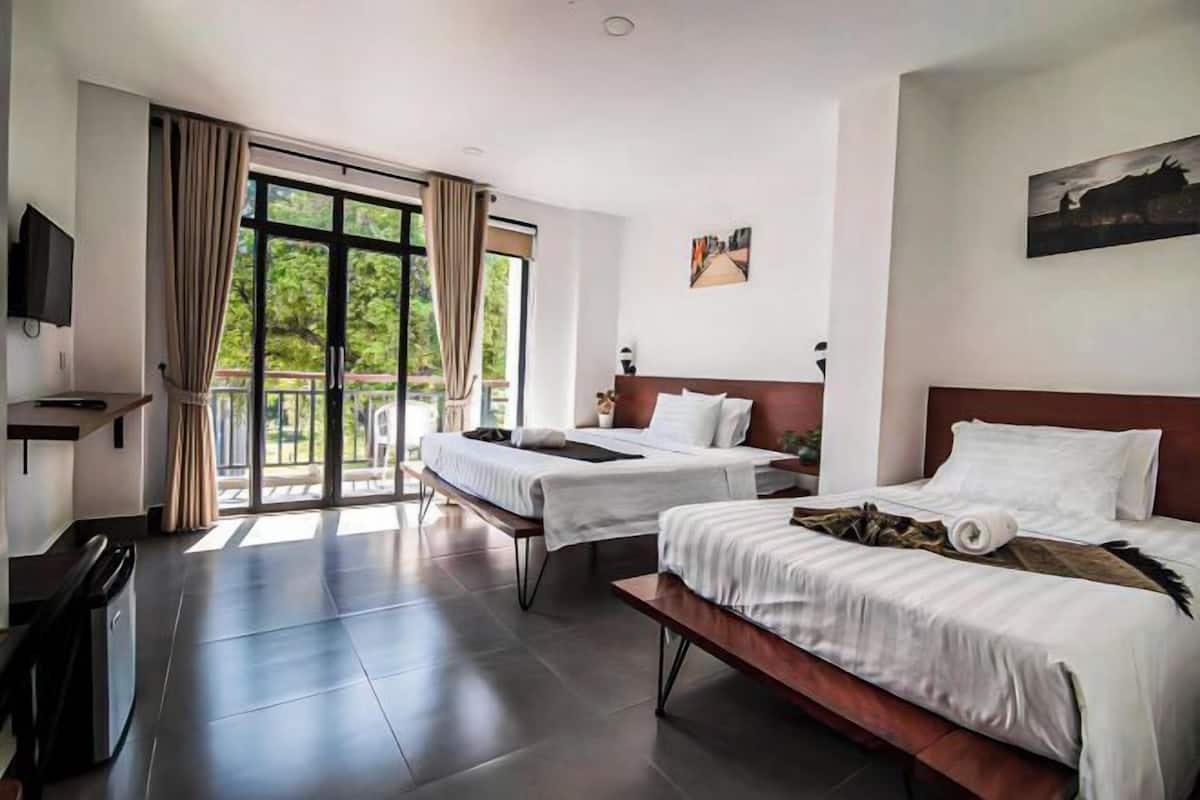 A hotel room with two beds, a TV, a balcony, and a painting on the wall.
