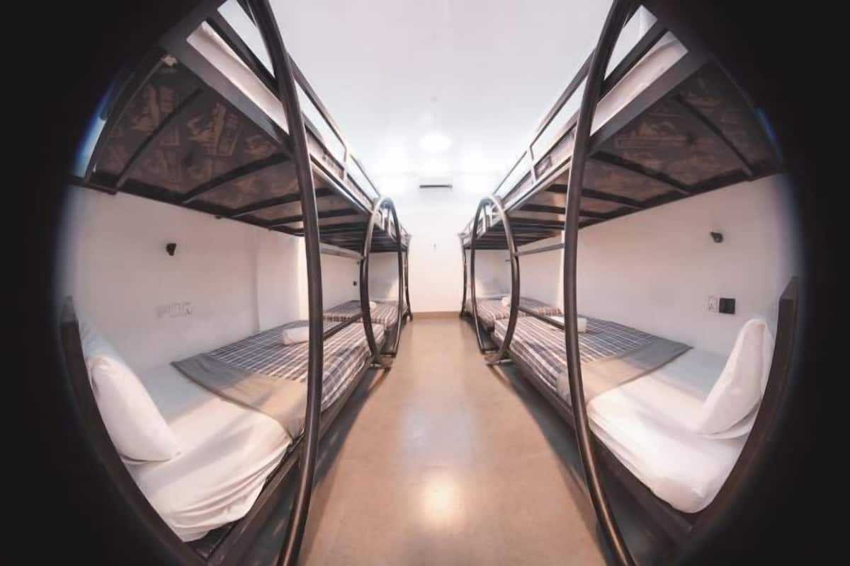 A corridor with bunk beds, a central light fixture, and a plain wall.