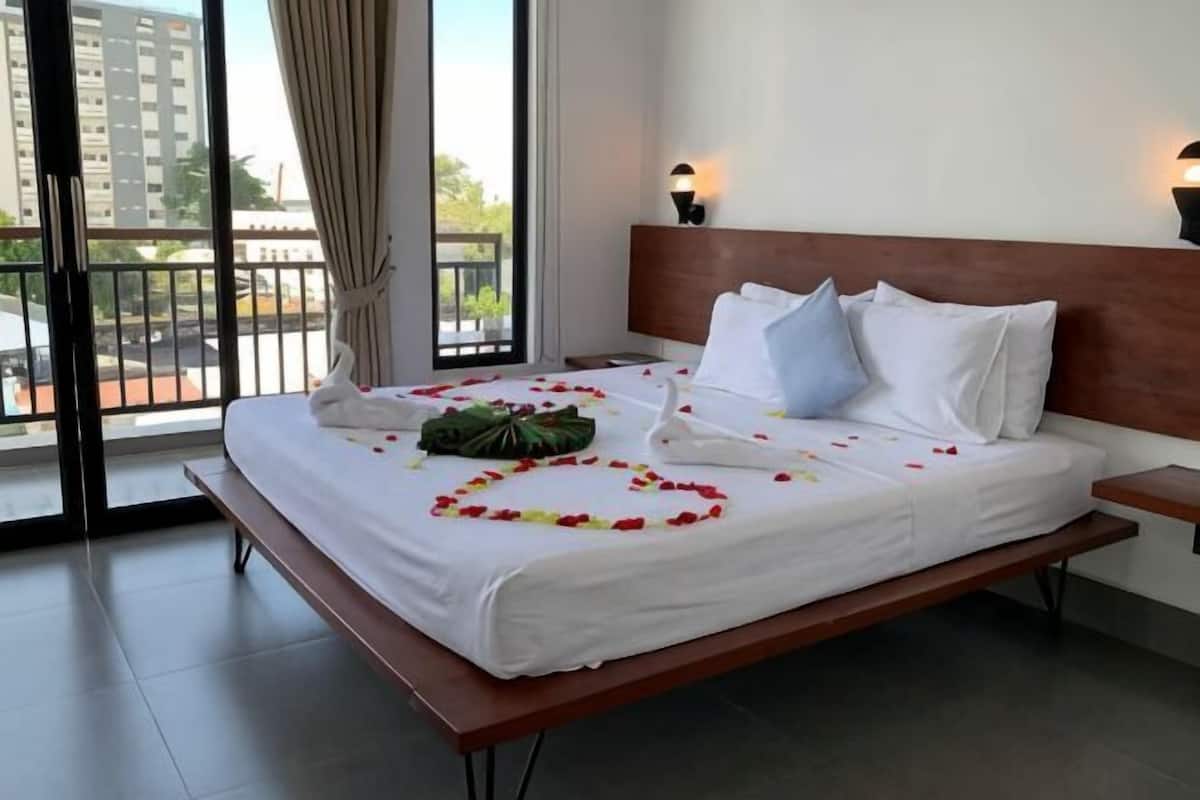 A hotel room with a bed, a nightstand, a window with curtains, and a view of buildings outside.