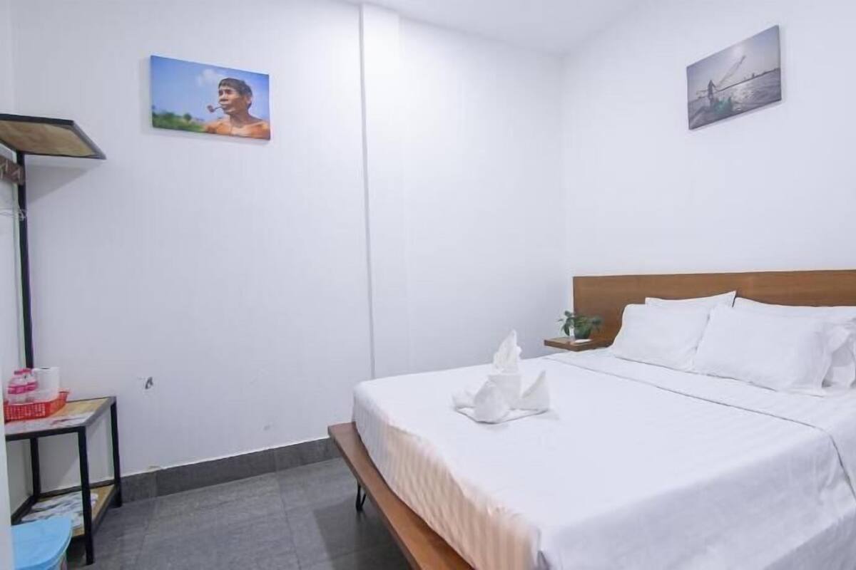 A hotel room with a bed, a bedside table with a plant, and two wall-mounted pictures.