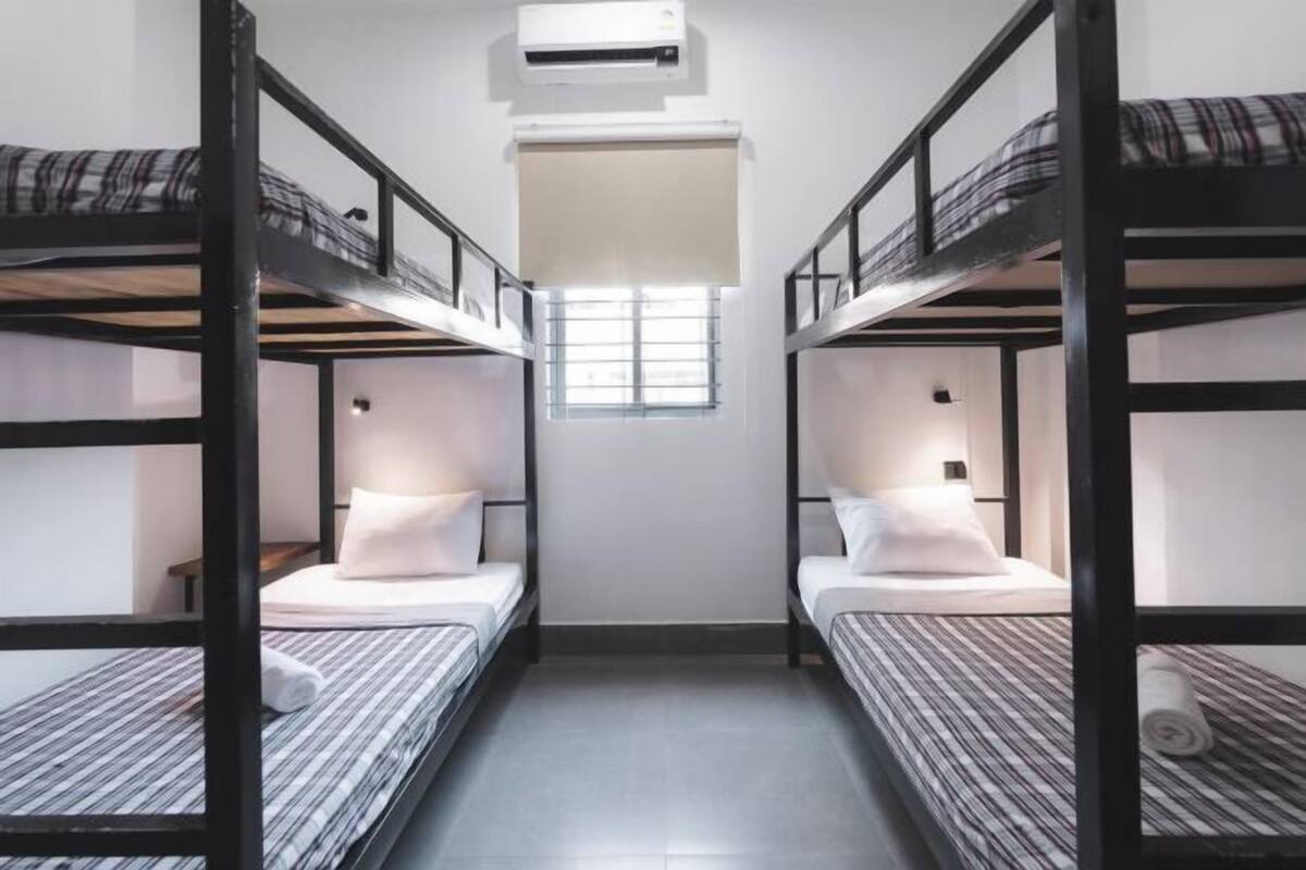 A narrow room with bunk beds, a window with blinds, and an air conditioning unit.