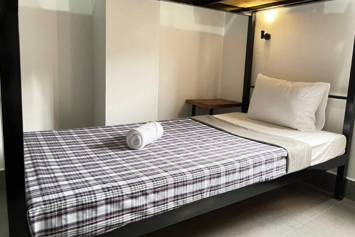 A single bed with a plaid bedspread and a white pillow in a room with a wooden ceiling and white walls.