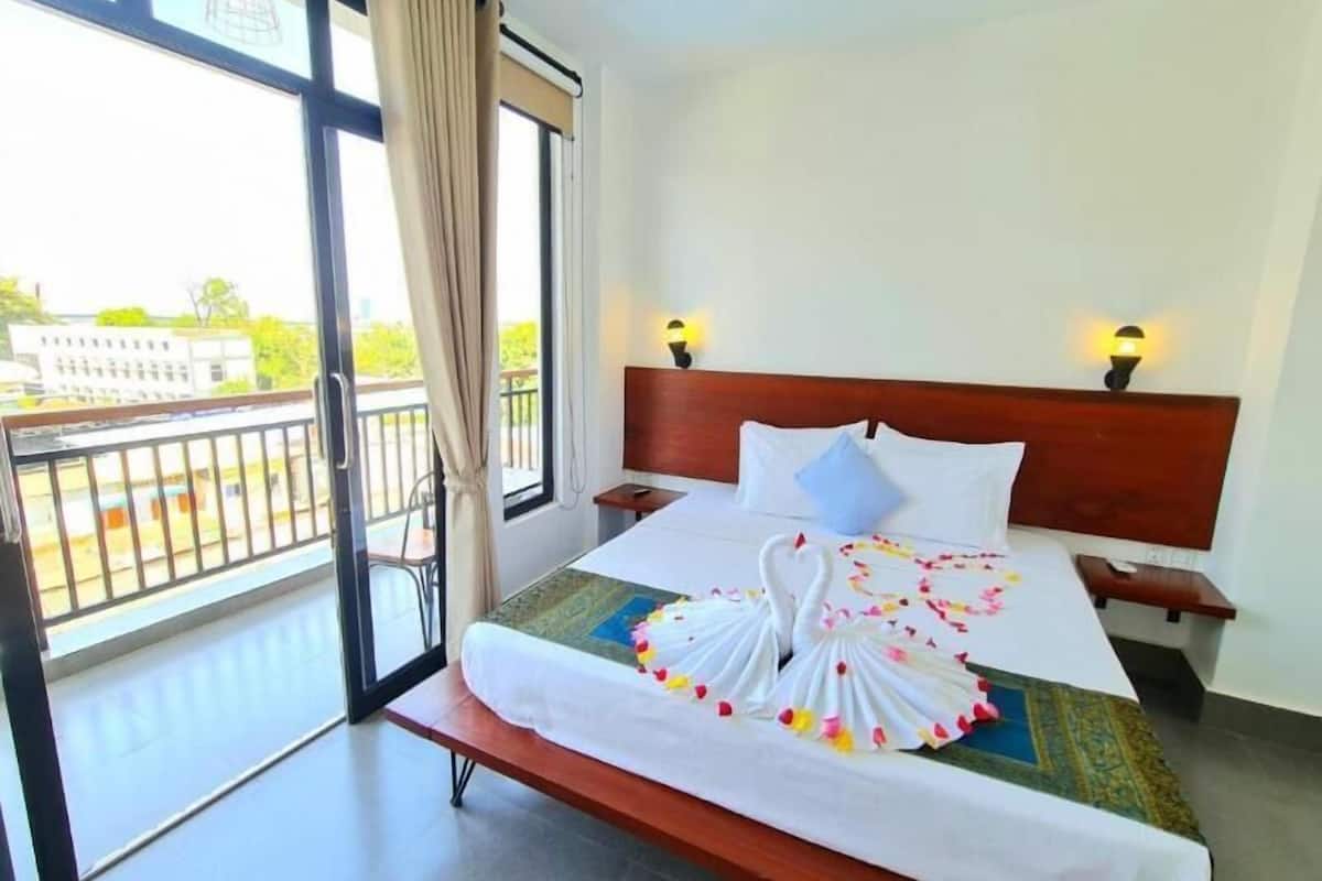 A hotel room with a bed, two bedside lamps, a view of the outside, and a balcony.