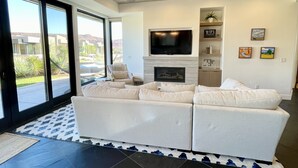 Un salon moderne doté d’un grand canapé d’angle, d’un téléviseur à écran plat, d’une cheminée et d’un ventilateur de plafond.