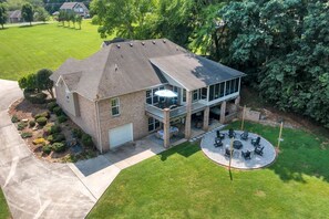 A two-story house with a covered patio, a lawn, and a circular seating area.