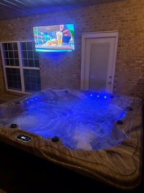 Un jacuzzi doté de lumières LED bleues, un téléviseur fixé au mur et un mur en briques.