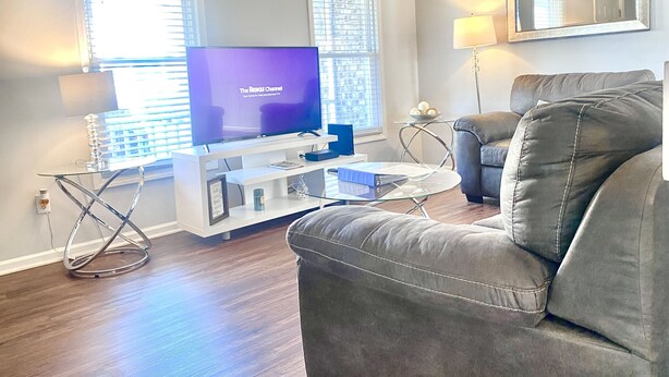 Een woonkamer met een flatscreen televisie, een grijze bank, een glazen salontafel en een lamp.