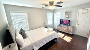 Een slaapkamer met een bed, een plafondventilator, een dressoir, een televisie en een deur.