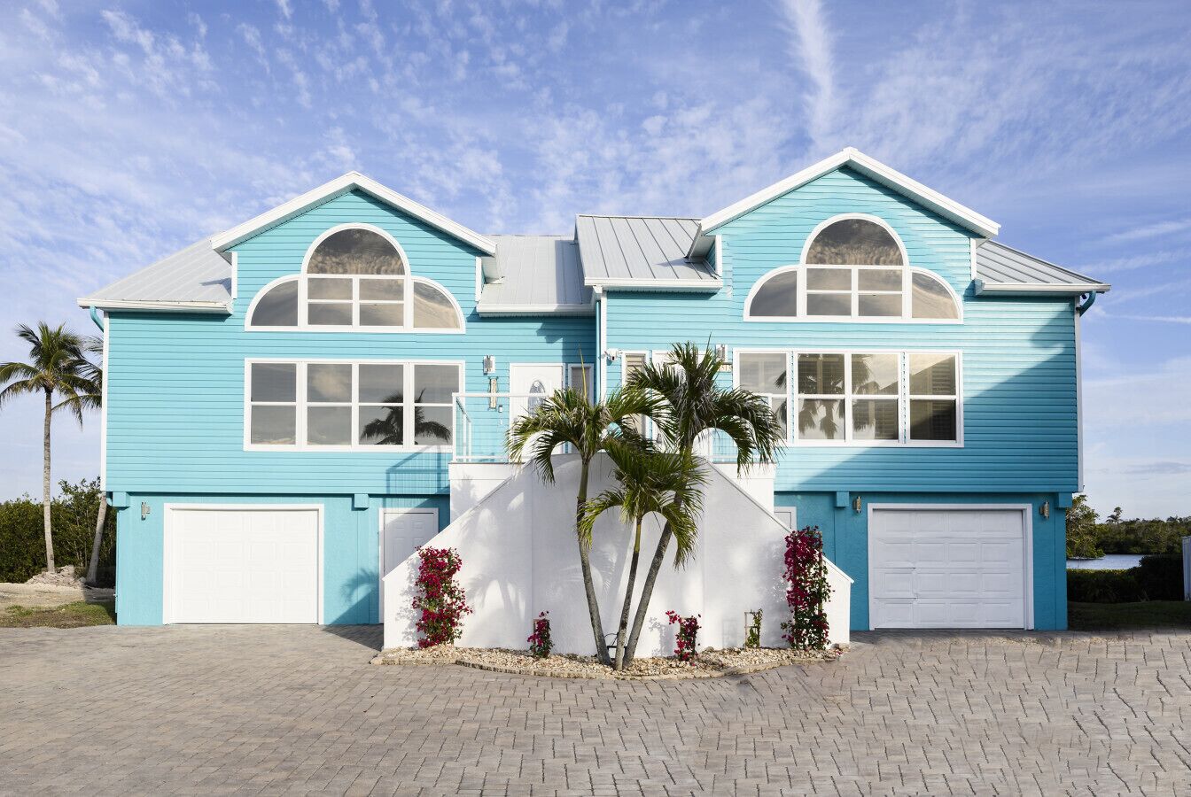 Una casa de dos pisos con fachada azul claro, detalles blancos y un garaje en la parte frontal.