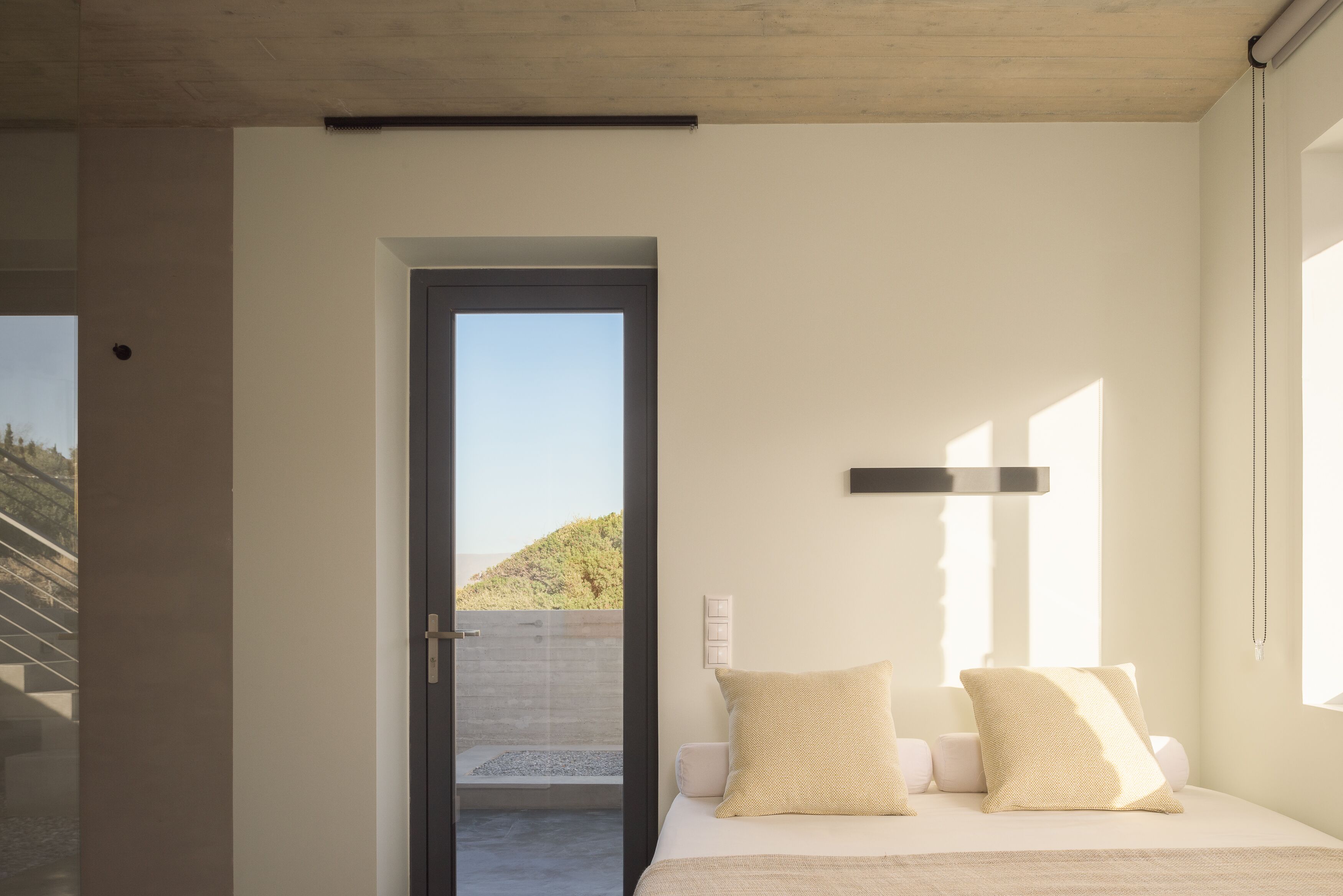 Une chambre à coucher moderne avec un lit, une porte donnant sur un balcon et une vue sur une colline.