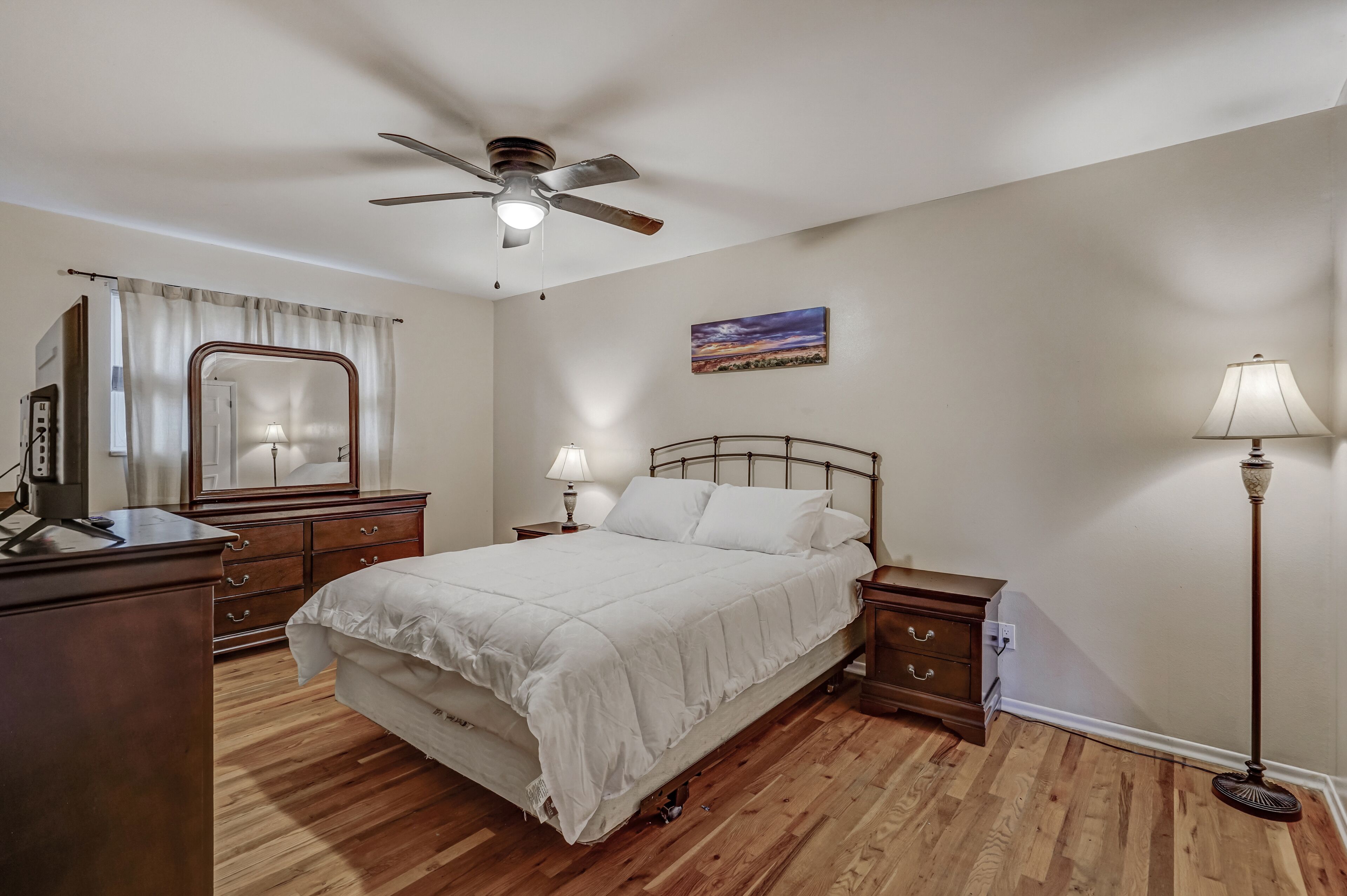 Une chambre à coucher comprenant un lit, un ventilateur de plafond, une table de chevet, une lampe, une commode et un miroir.