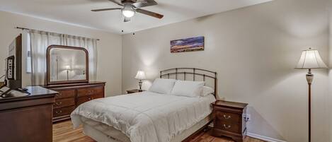 Une chambre à coucher comprenant un lit, un ventilateur de plafond, une table de chevet, une lampe, une commode et un miroir.