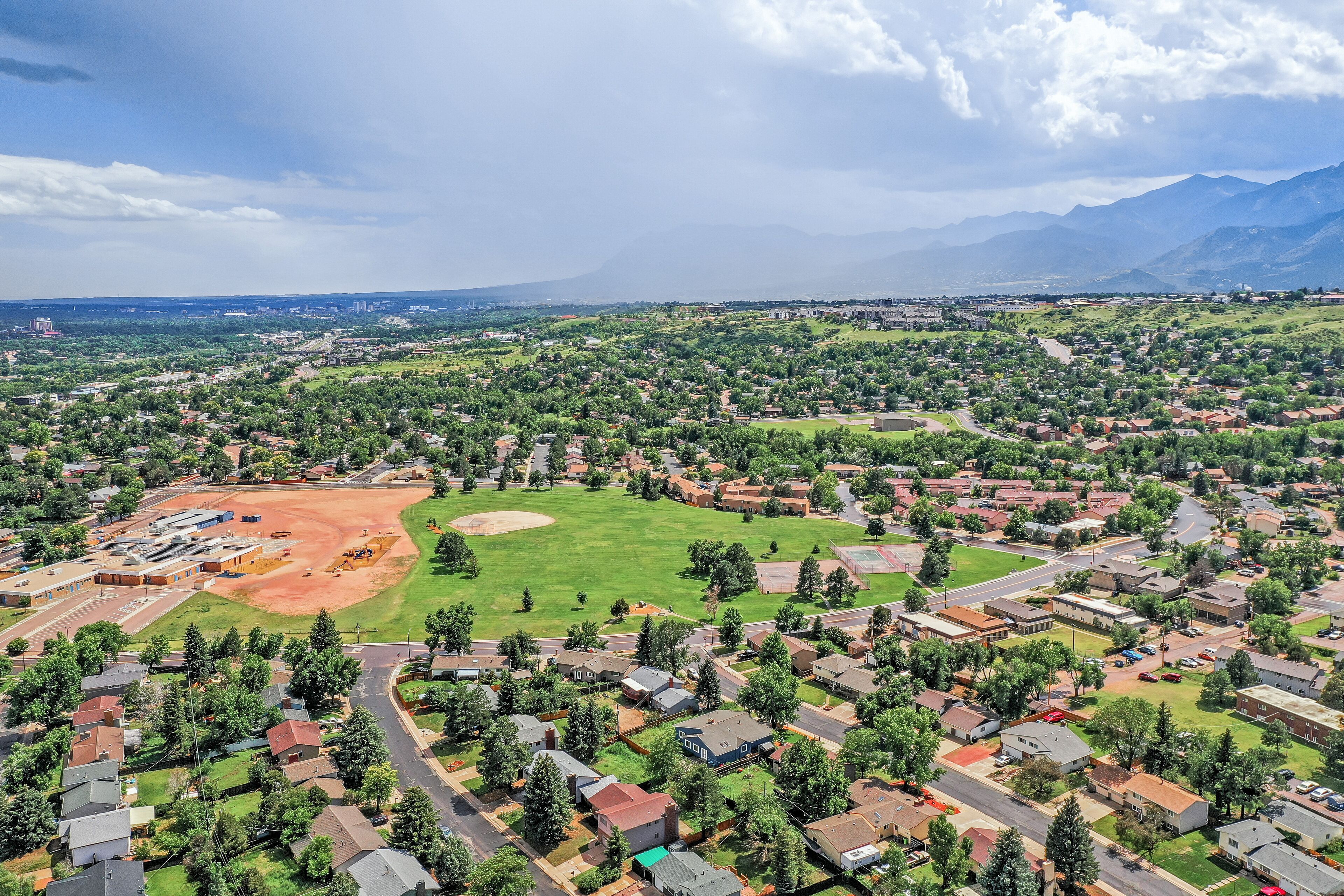 An aerial view of a residential area with houses, a baseball field, and mountains in the background.