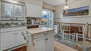 A kitchen with white cabinets, a wooden countertop, and a dining area with a table and chairs. - Sherwood (Colorado Springs)