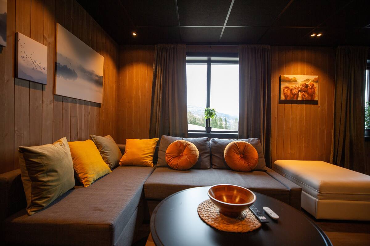 Ein gemütliches Zimmer mit einer Couch, Kissen, einem runden Tisch mit einer Schale und Bildern an den Wänden.