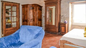 Une pièce avec un fauteuil bleu, des meubles en bois, une petite table et un lit avec un matelas blanc.