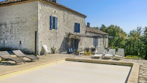 Un bâtiment en pierre doté d’un patio comprenant des chaises longues et une piscine.