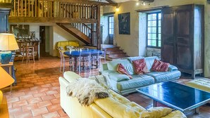 Un vaste espace de vie doté d’un haut plafond, d’un escalier, d’une table à manger avec des chaises, d’un canapé et d’un téléviseur.