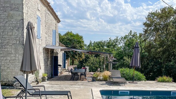 Un espace aménagé au bord de la piscine, avec des chaises longues, un patio couvert et un bâtiment en pierre.