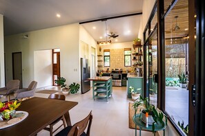 Enjoy a spacious open-plan living area with a dining table and comfortable seating, a well-equipped kitchen with a large island, and a view of the surrounding garden.