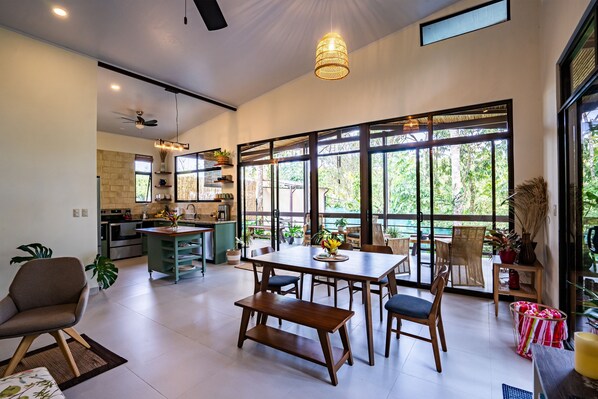 A spacious living area with a large dining table, comfortable seating, and a view of the outdoors through large windows.