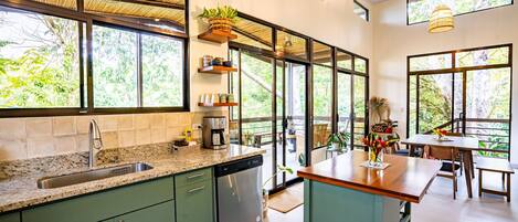 Cocina moderna con una isla grande, electrodomésticos integrados y amplios ventanales con vistas al verdor.