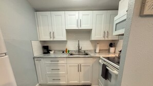 Una cocina compacta con armarios blancos, horno integrado y microondas.