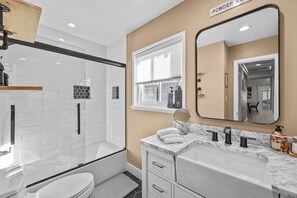 Une salle de bain moderne dotée d’une douche à parois de verre, d’un meuble-lavabo avec un plan de travail en marbre et d’un grand miroir.