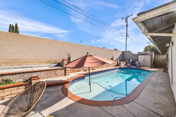 Une piscine bordée de briques, une chaise longue et un parasol de patio.