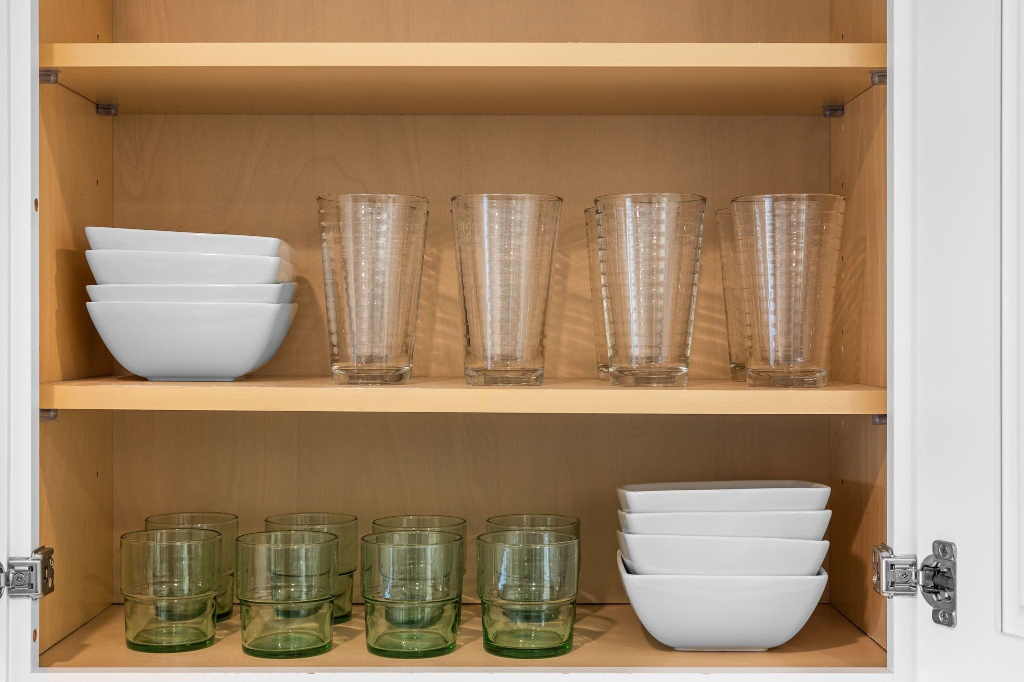 A cabinet with shelves containing white bowls and clear glassware.