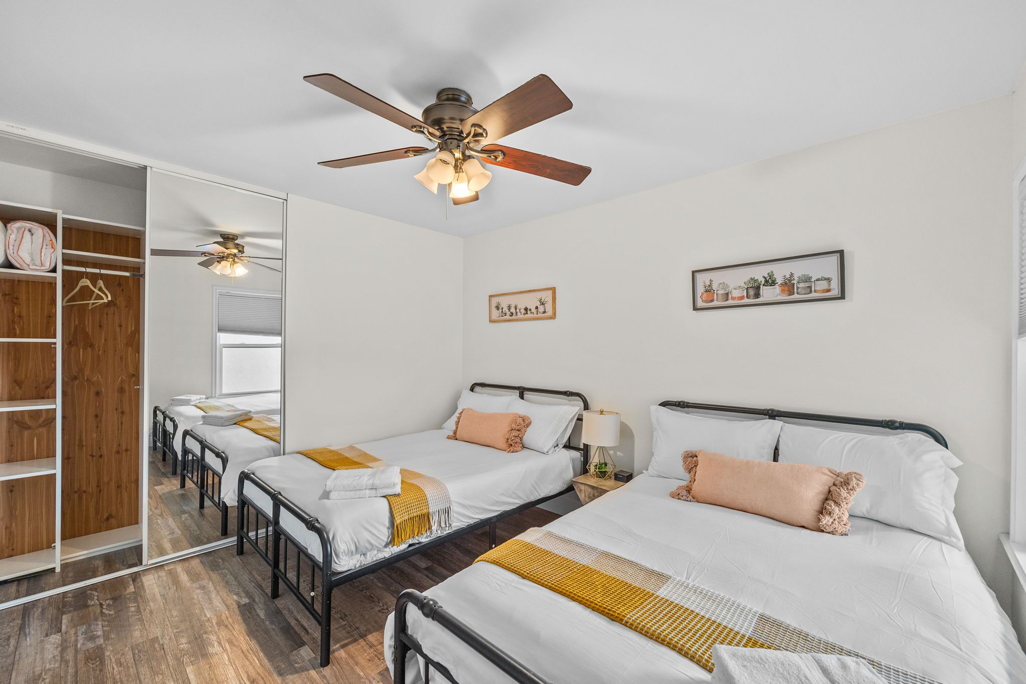 A hotel room with two single beds, a wardrobe, a ceiling fan, and a mirror.